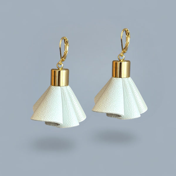 Boucles d'oreilles dorées en pompons frou frou de cuir blanc cassé nacré, debout sur fond gris