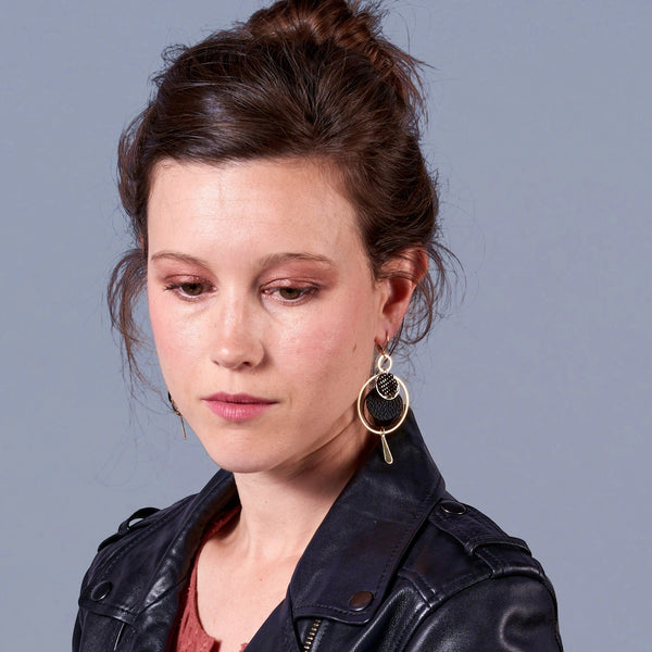 Jeune femme à chignon et perfetto portant les Boucles d'oreilles dorées Nune modèle Galassia en cuirs noir grainé et noir grainé irisé