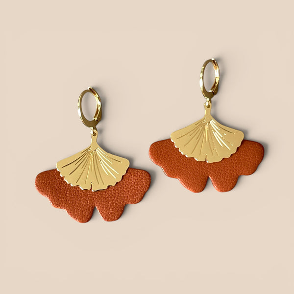 Boucles d'oreilles dorées pendantes en cuir terracotta en forme de gingko, sur fond beige