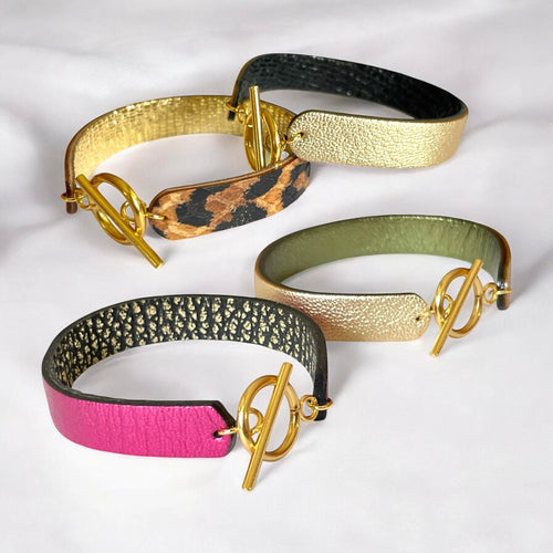 4 bracelets en cuir double face bicolores, avec fermoir boucle dorée en T, en cuirs fushia métallisé et noir grainé or pour le 1er, et doré antique mat et kaki métallisé pour le second, noir brillant façon serpent, doré antique mat pour le 3e et cuirs façon léopard et doré façon serpent pour le 4e, sur fond gris clair