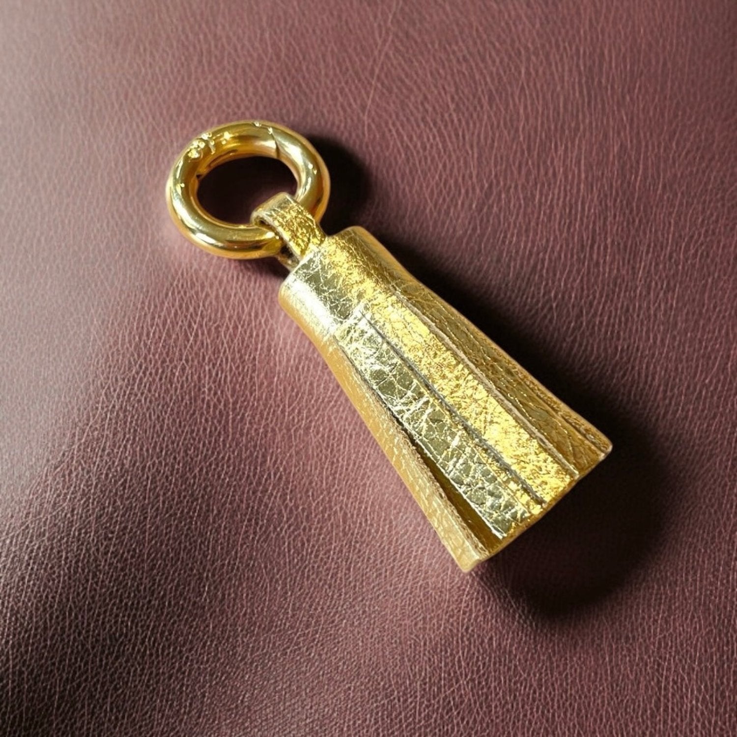 porte-clé doré en cuir doré , en forme de pompon, sur fond cuir marron