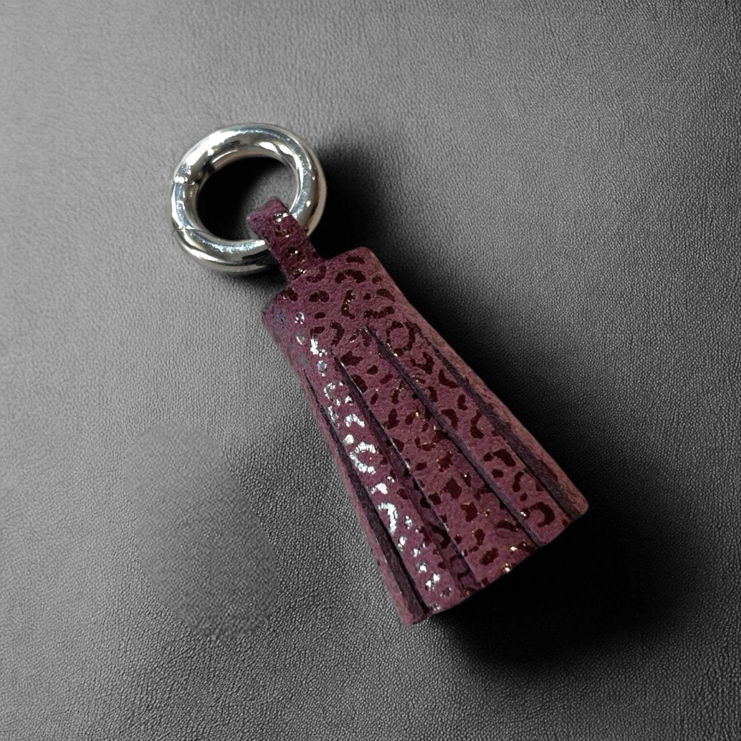 porte-clé argent en cuir prune motif léopard , en forme de pompon, sur fond noir