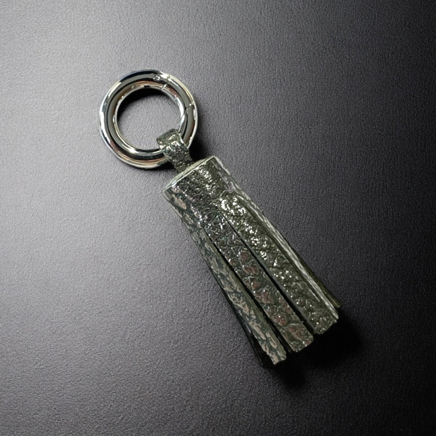 porte-clé argent en cuir gris kaki grainé argent, en forme de pompon, sur fond noir