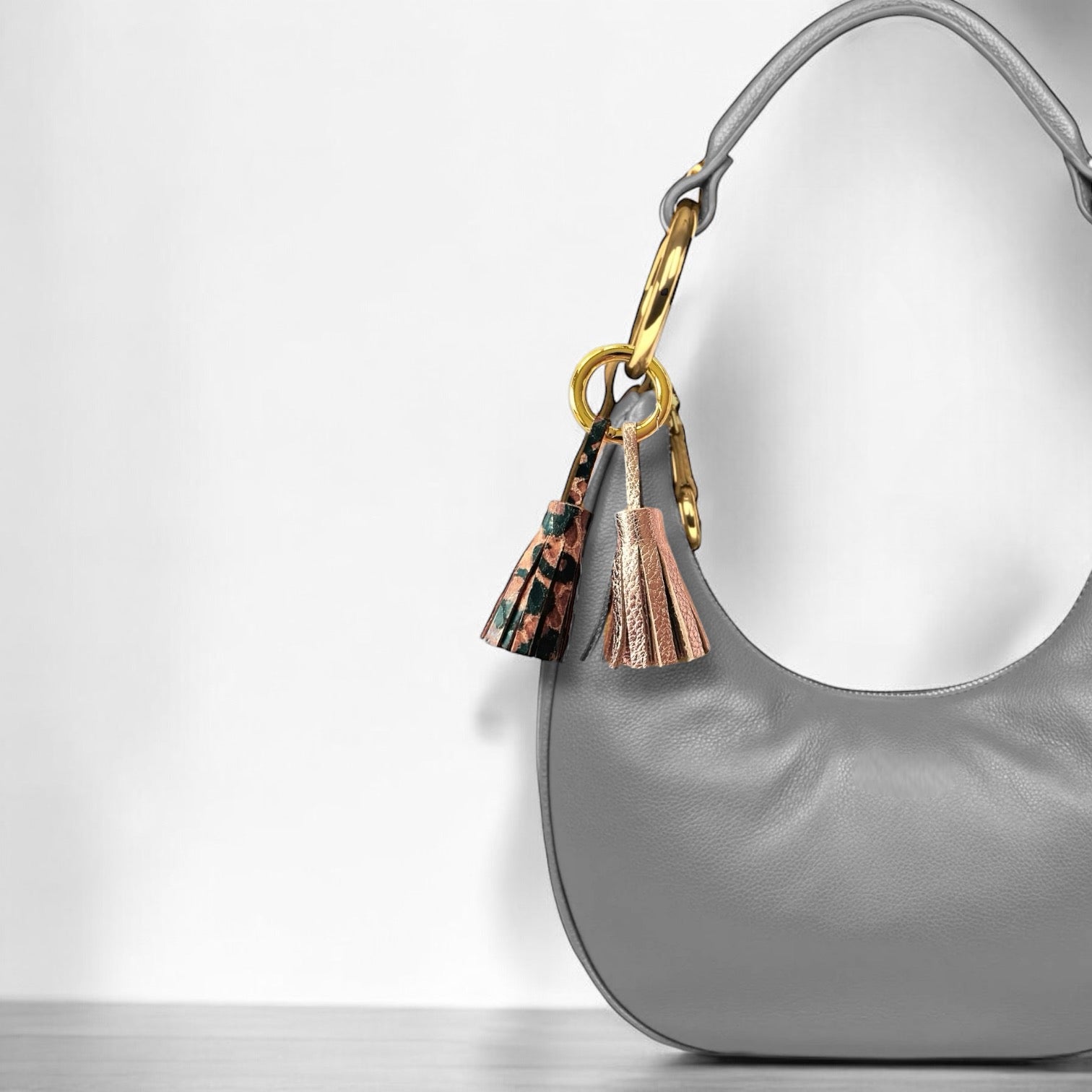 Bijou de sac doré avec 2 pompons en cuirs rose pâle métallisé et façon léopard, accroché sur le côté d'un sac à main gris