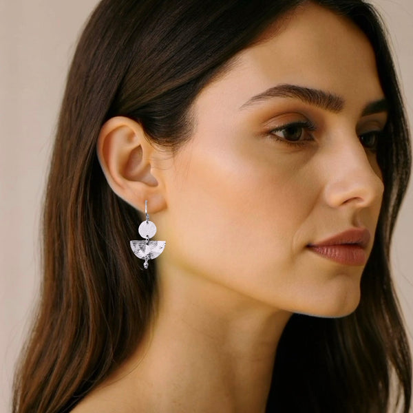 Petites boucles d'oreilles argentées pendantes en forme de demi-lunes, portées aux oreilles