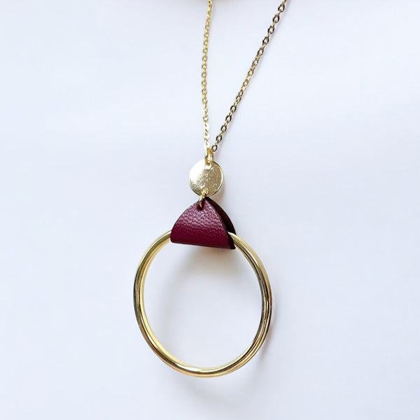 Collier fin dorée avec pendentif grand anneau créole attaché par une fine pièce de cuir pourpre, sur fond blanc