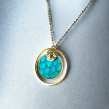 Charger l&#39;image dans la galerie, Fin collier doré avec pendentif rond en anneau avec une pièce de cuir marin bleu turquoise brut, sur fond argenté
