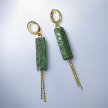 Charger l&#39;image dans la galerie, Boucles d&#39;oreilles Effinis de Nune, dorées à l&#39;or fin avec cuir marin, cuir de poisson saumon vert bouteille métallisé, de forme effilée avec chaînettes dorées pendantes, sur fond cuir gris argenté
