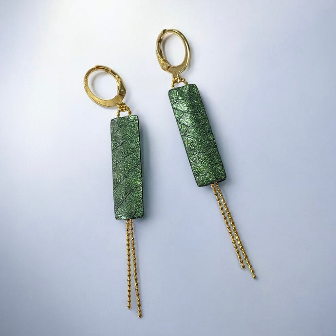 Boucles d'oreilles Effinis de Nune, dorées à l'or fin avec cuir marin, cuir de poisson saumon vert bouteille métallisé, de forme effilée avec chaînettes dorées pendantes, sur fond cuir gris argenté