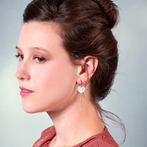 Jeune femme brune avec un chignon portant une boucle d'oreille à fines chaînettes pendantes, en forme de cœur en cuir blanc cassé nacré