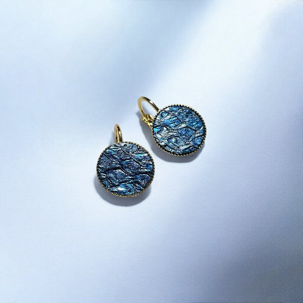 Petites boucles d'oreilles dormeuses dorées serties de fin cuir marin saphir métallisé, sur fond bleu