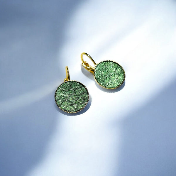 Petites boucles d'oreilles dormeuses dorées serties de fin cuir marin vert bouteille métallisé, sur fond bleu