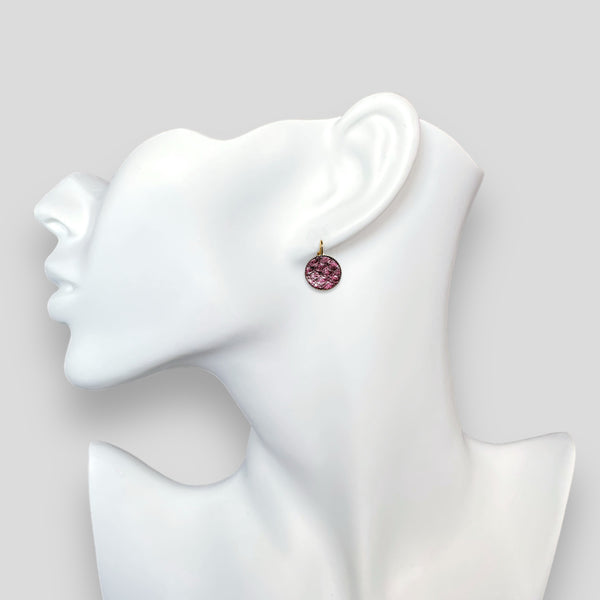 Petites boucles d'oreilles dormeuses dorées serties de fin cuir marin grenat métallisé, portées à l'oreille sur un buste blanc