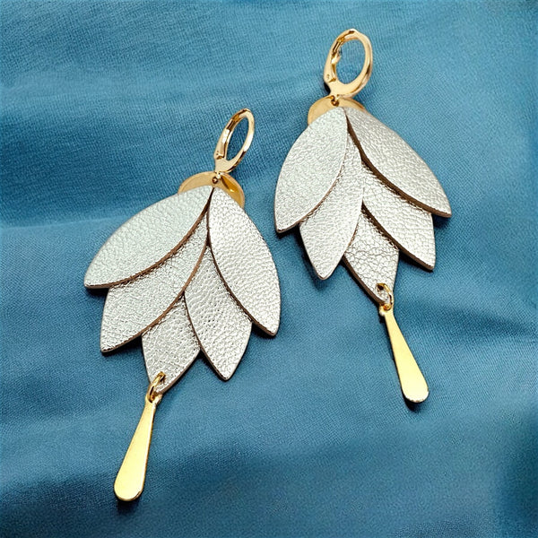Boucles d'oreilles dorées pendantes Nune modèle Nymphéa en cuir argent , sur fond de tissu bleu