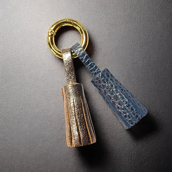 Bijou de sac doré avec 2 pompons en cuirs cannelle dorée satinée et gris mordoré grainé, sur fond noir