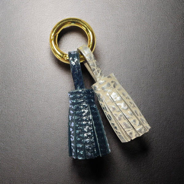 Bijou de sac doré avec 2 pompons en cuirs bleu glacier métallisé grainé et argent grainé, sur fond noir