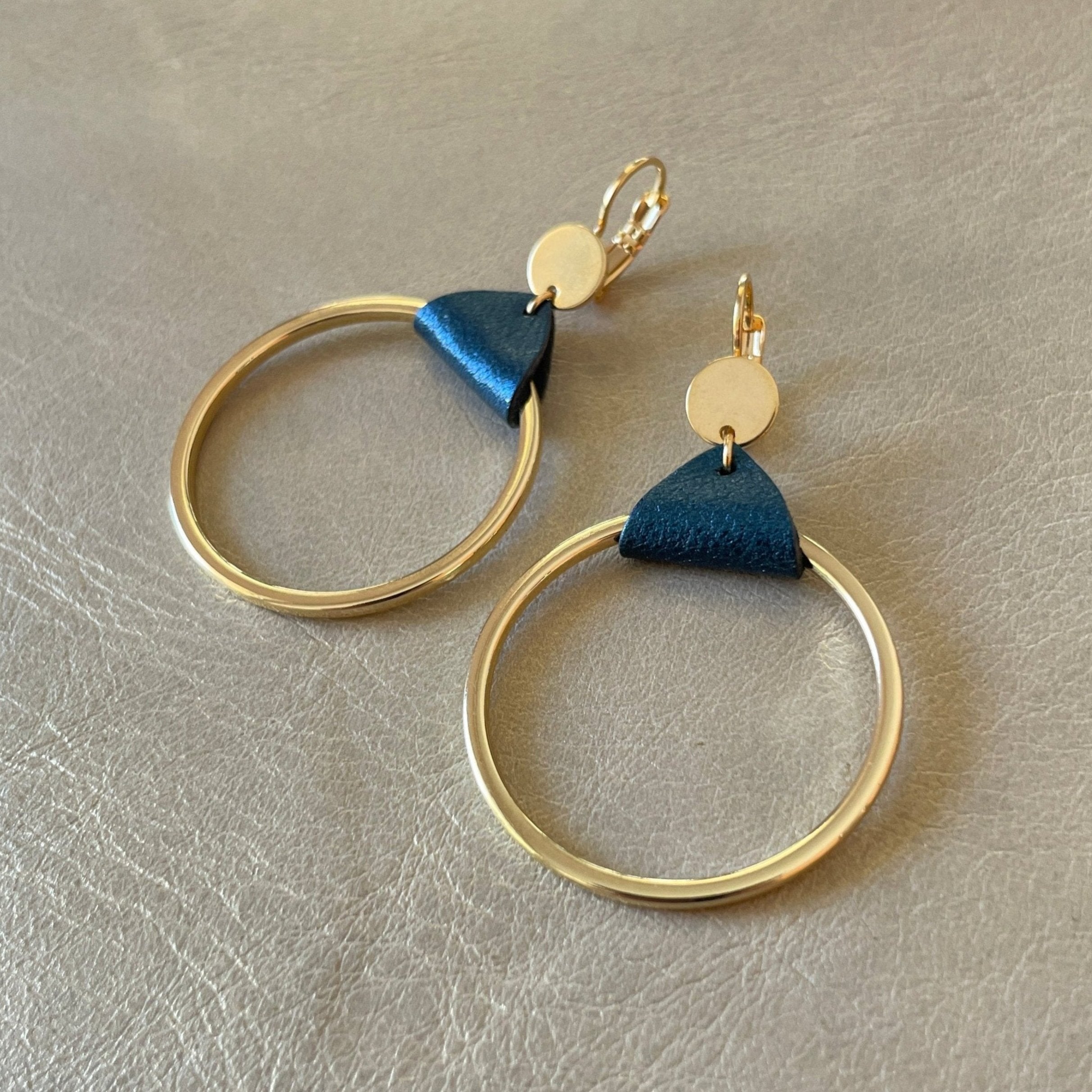 Boucles d'oreilles dorées, grands anneaux créoles, noués par un morceau de cuir bleu nuit métallisé aux accroches dormeuses, présentées sur fond gris