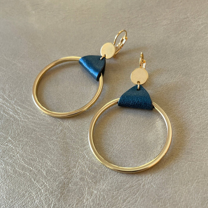 Boucles d'oreilles dorées, grands anneaux créoles, noués par un morceau de cuir bleu nuit métallisé aux accroches dormeuses, présentées sur fond gris