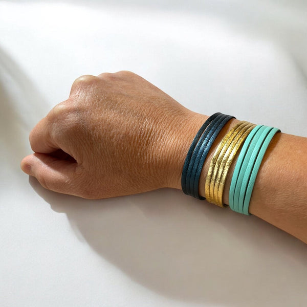3 bracelets à 4 liens en cuirs doré, bleu nuit métallisé et vert menthe, portés au poignet sur fond blanc