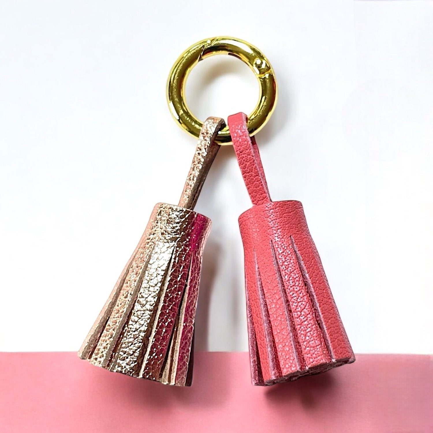 Bijou de sac doré avec 2 pompons en cuirs rose pâle métallisé et rose, sur fond blanc et rose pastel