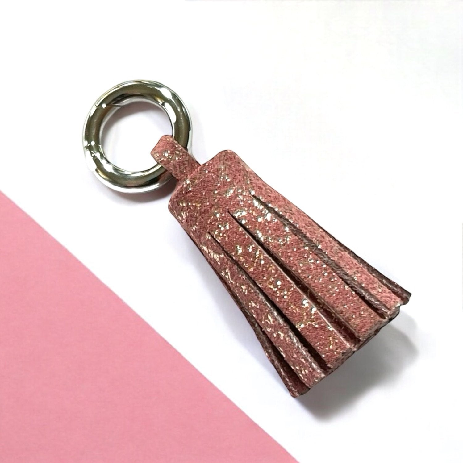 porte-clé argent en cuir vieux rose pailleté or, en forme de pompon, sur fond blanc et rose pastel