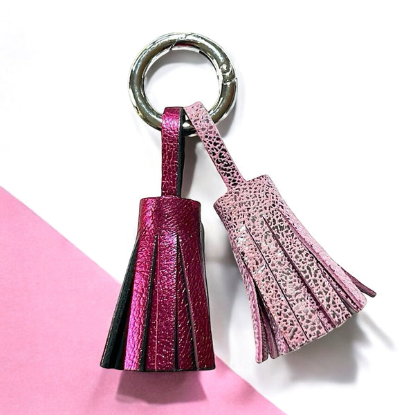 Bijou de sac argenté avec 2 pompons en cuirs fushia métallisé et rose brillant, sur fond blanc et rose pastel