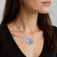 Charger l&#39;image dans la galerie, Collier argenté court avec pendentif en cuir bleu gris nacré en forme de fleur, porté au cou d&#39;une femme brune
