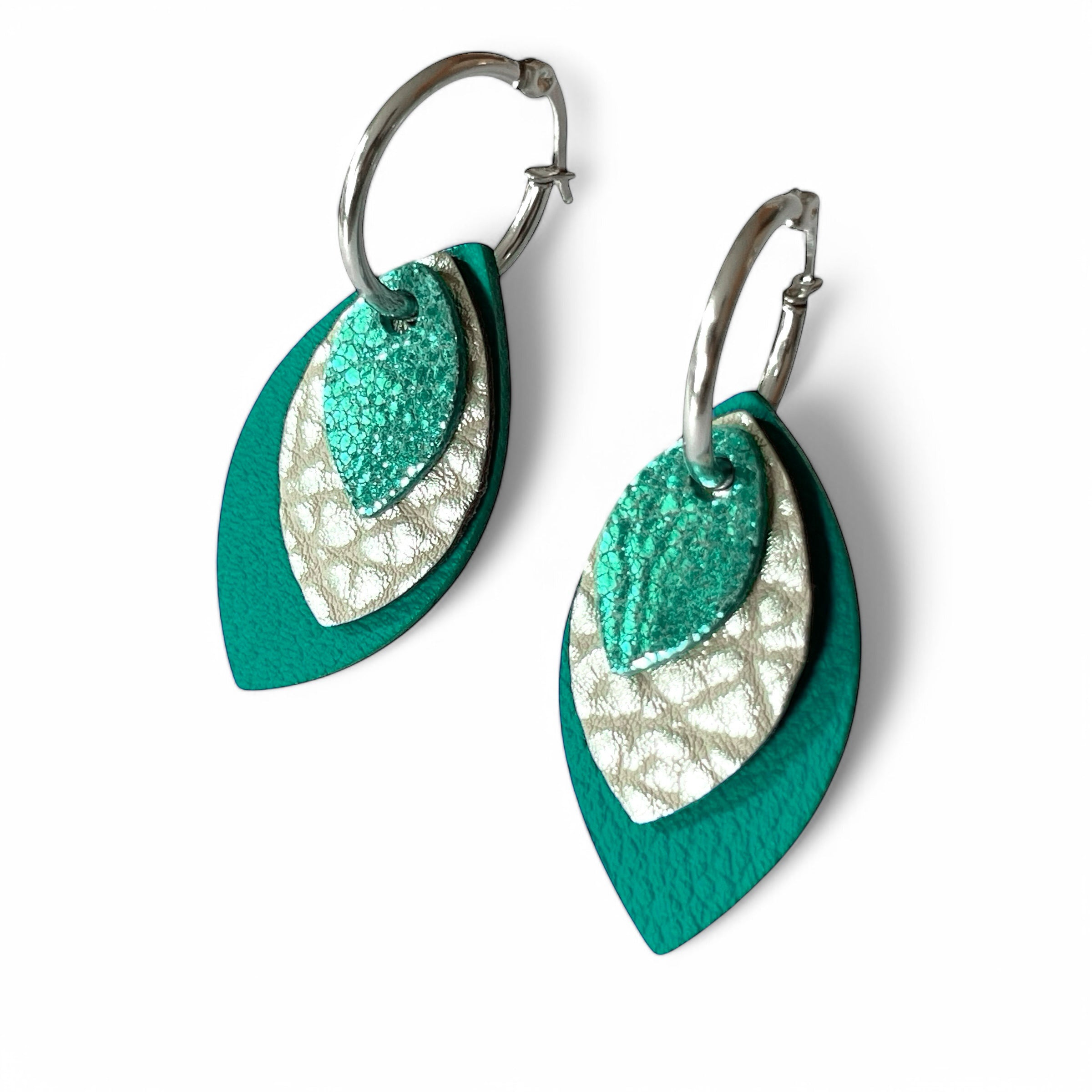 Créoles argentées avec pendentifs modulables en forme de feuilles en cuirs vert émeraude métallisé, argent grainé et vert émeraude grainé, sur fond blanc