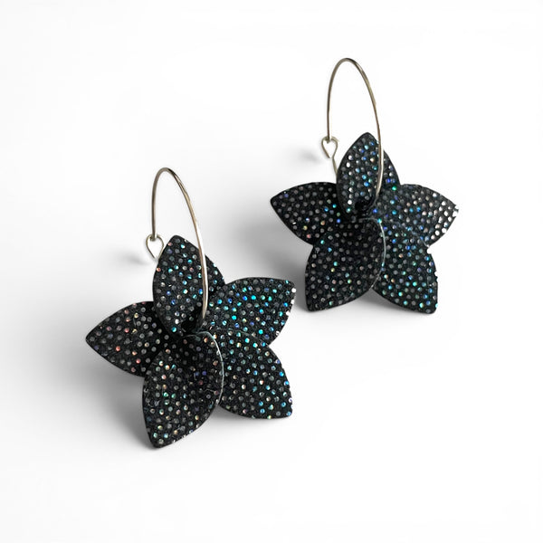 Petites boucles d'oreilles en forme de fleurs en cuir noir à pois holographiques, montées sur créoles argentées, sur fond blanc