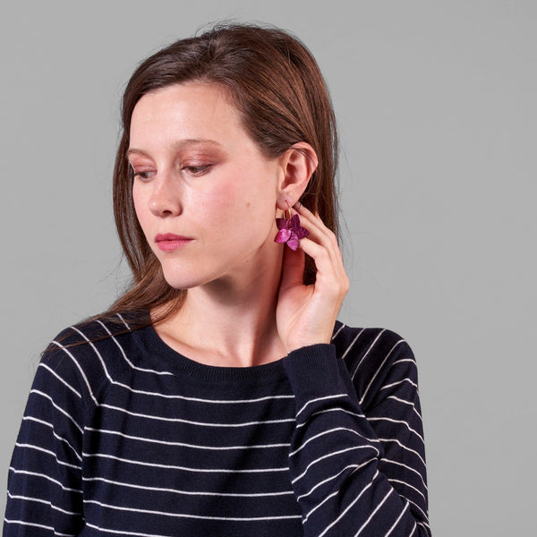 Jeune femme vue de 3/4 portant les petites créoles Jasmin en pétales de cuir fushia métallisé, en forme de fleurs, sur fond gris
