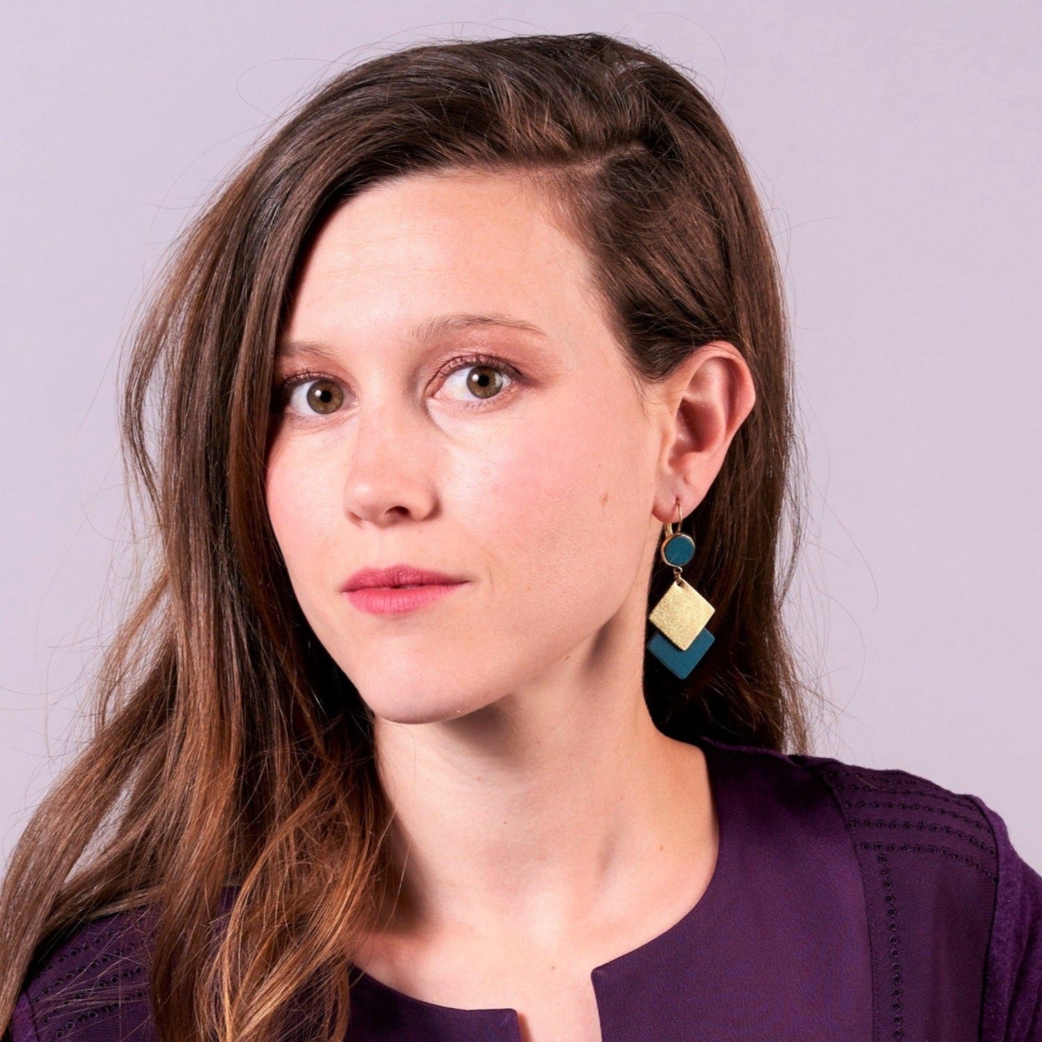 NUNE boucles d'oreilles Adalisa dorées avec cabochon en cuir vert canard et duo de losanges en cuir recyclé vert canard et doré portées par une jeune femme à longs cheveux bruns avec un haut violet