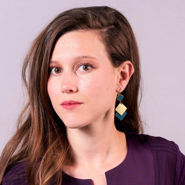 NUNE boucles d'oreilles Adalisa dorées avec cabochon en cuir vert canard et duo de losanges en cuir recyclé vert canard et doré portées par une jeune femme à longs cheveux bruns avec un haut violet