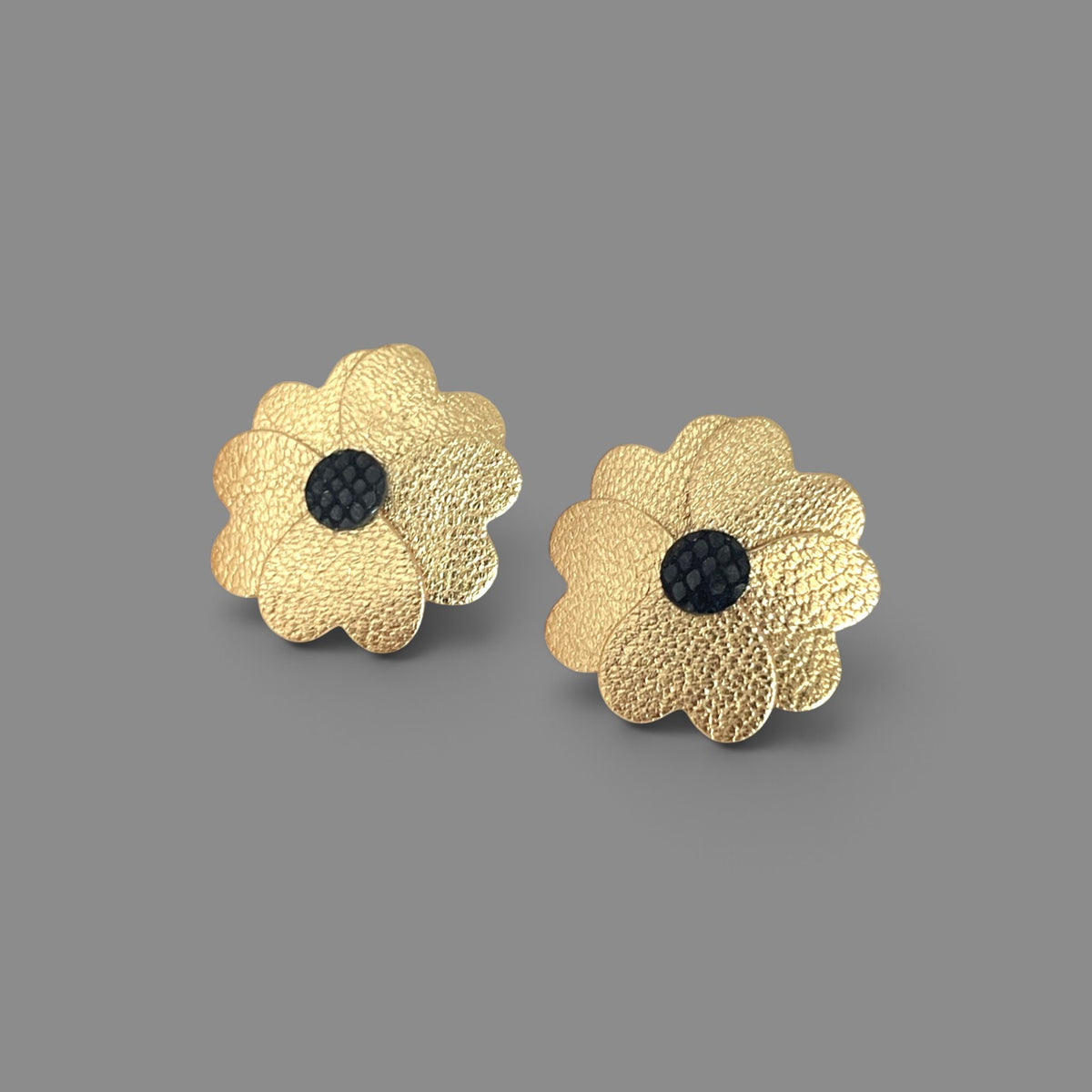 Boucles d'oreilles en forme de petites fleurs en cuirs doré satiné et noir petit grain irisé, sur fond gris