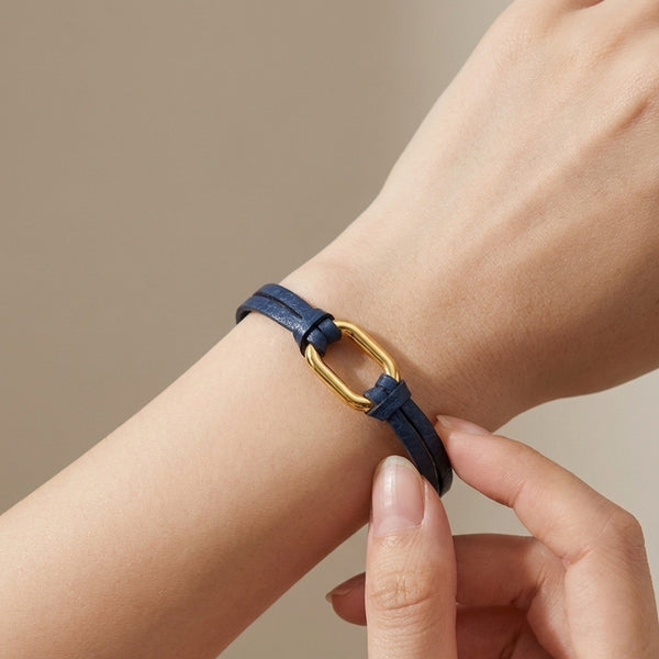 Bracelet à boucle dorée en fins liens de cuir bleu marine, avec fermoir aimanté doré, porté au poignet