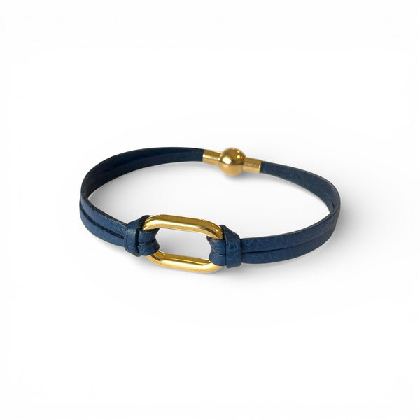 Bracelet à boucle dorée en fins liens de cuir bleu marine, avec fermoir aimanté doré, sur fond blanc