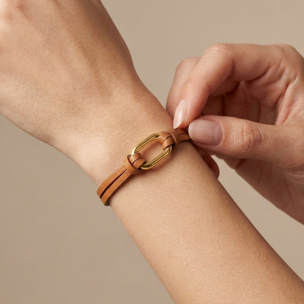 Bracelet à boucle dorée en fins liens de cuir camel, avec fermoir aimanté doré, porté au poignet