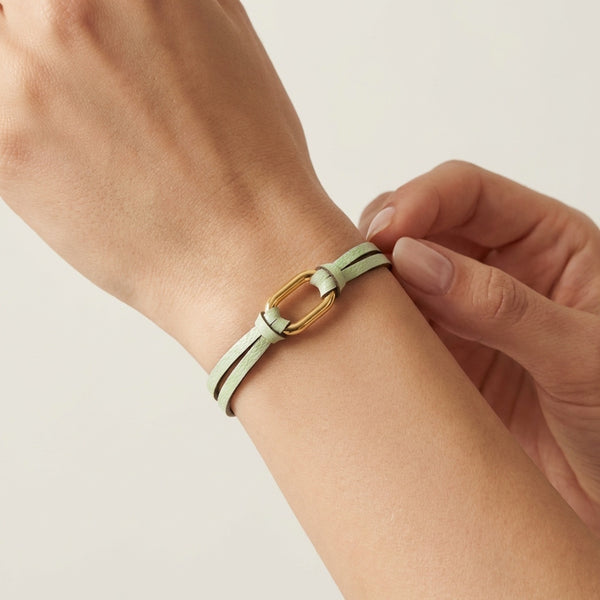 Bracelet à boucle dorée en fins liens de cuir vert d'eau, avec fermoir aimanté doré, porté au poignet