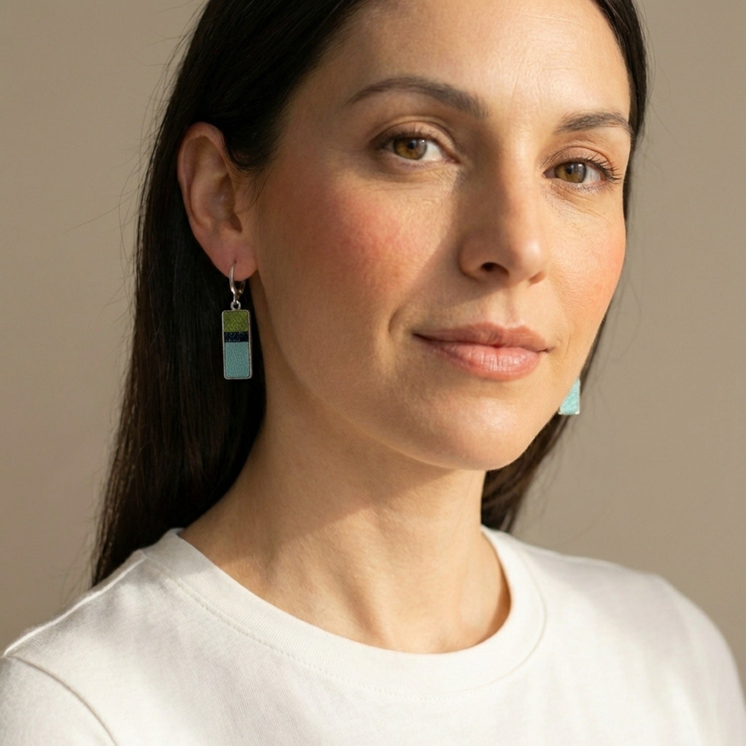 Petites boucles d'oreilles argentées pendantes rectangulaires verticales tricolores en cuirs kaki métallisé, noir à pois holographiques et bleu gris nacré, portées aux oreilles par une femme brune