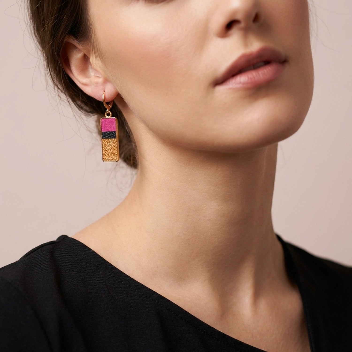 Petites boucles d'oreilles dorées pendantes rectangulaires verticales tricolores en cuirs rose fushia, noir petit grain irisé et cuivre clair, portées au oreilles par une femme brune aux cheveux attachés