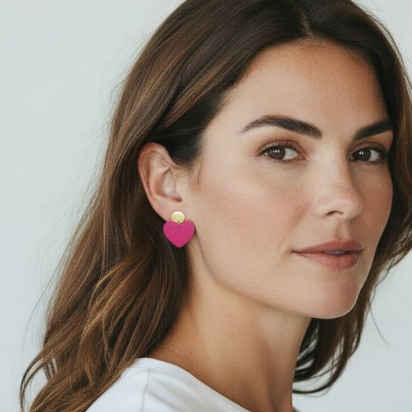 NUNE puces d'oreilles dorées Mims avec pendentifs cœurs en cuir rose fuschia recyclé portées aux oreilles par une femme brune