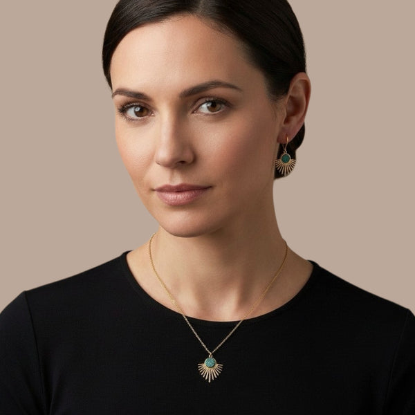 Collier doré fin avec pendentif en forme de petit soleil, avec cabochon de cuir coloré revalorisé bleu paon pailleté, porté par une femme brune, qui porte aussi aux oreilles les boucles d'oreilles dorées Miria assorties au collier