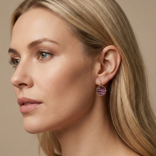 Petites boucles d'oreilles dormeuses dorées serties de fin cuir marin grenat métallisé, portées à l'oreille par une femme blonde
