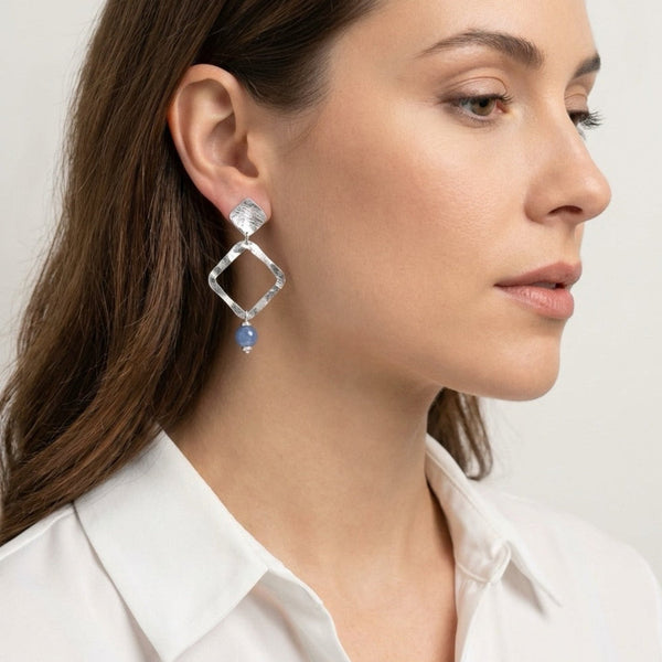 Boucles d'oreilles losanges montées sur puces en métal martelé argenté et perles d'aventurine bleu ciel, portées à l'oreille par une femme brune