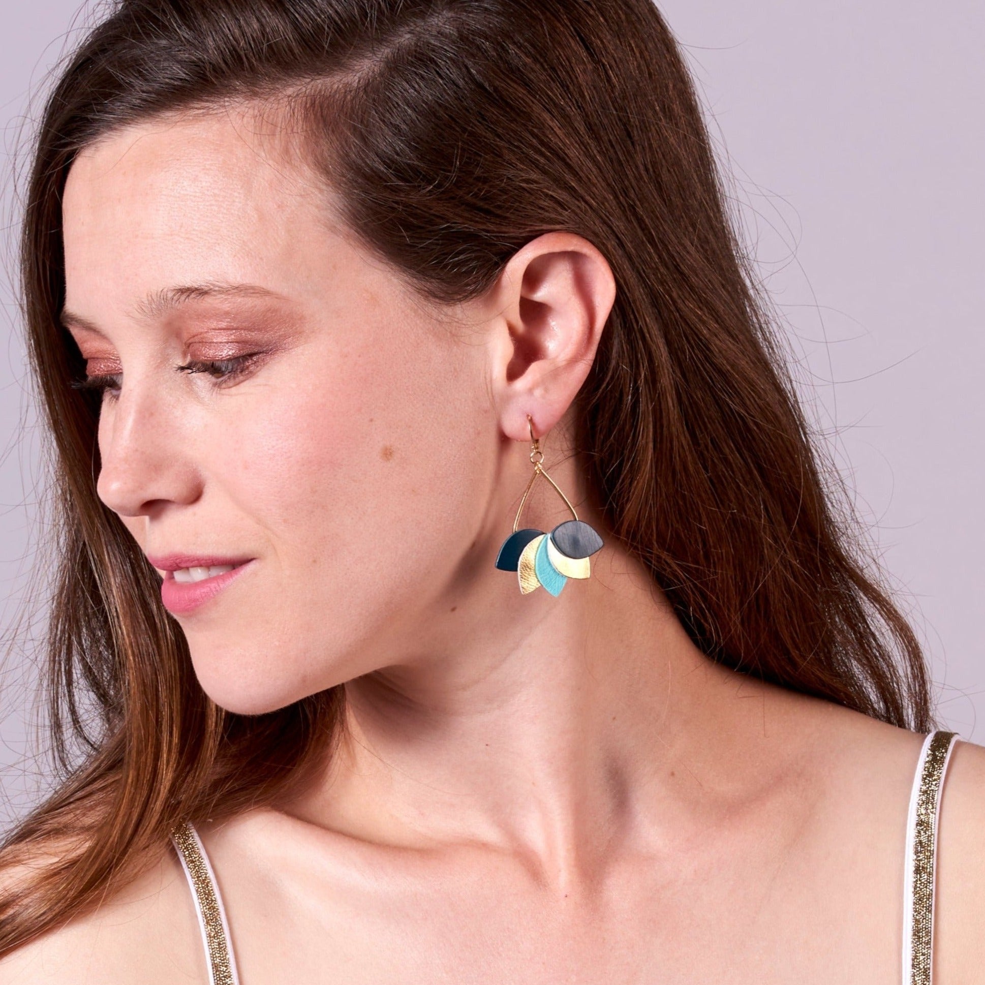 Jeune femme vue de profil portant les Boucles d'oreilles Nune modèle Aponi dorées à l'or fin avec pétales de cuir vert canard, doré brillant et vert menthe satiné, en forme de couronne de pétales