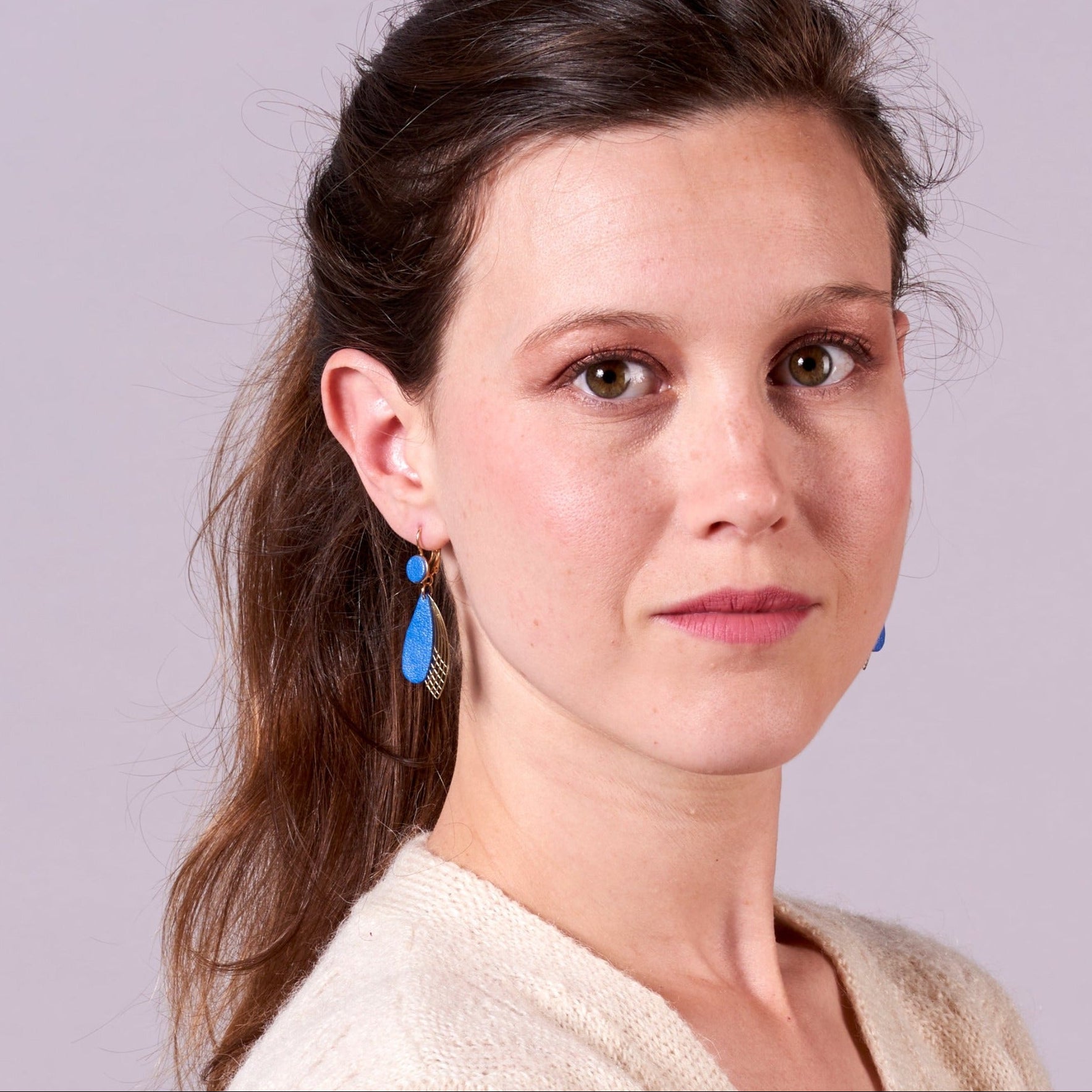 Jeune femme portant les Boucles d'oreilles dorées Nune modèle Pétales en cuir bleu pervenche nacré