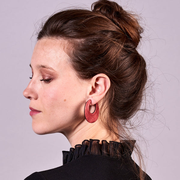 Jeune femme à chignon vue de profil portant les grandes boucles d'oreilles créoles rondes tout-cuir Circus, vues du côté rubis métallisé