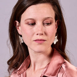 Jeune femme vue de face et en buste portant les petites créoles Jasmin en pétales de cuir fushia métallisé, en forme de fleurs, sur fond mauve