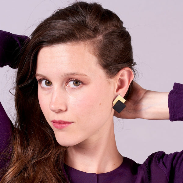 Jeune femme vue de près portant les boucles d'oreilles puces Adalis, duo de losanges en cuir recyclé noir satiné et doré