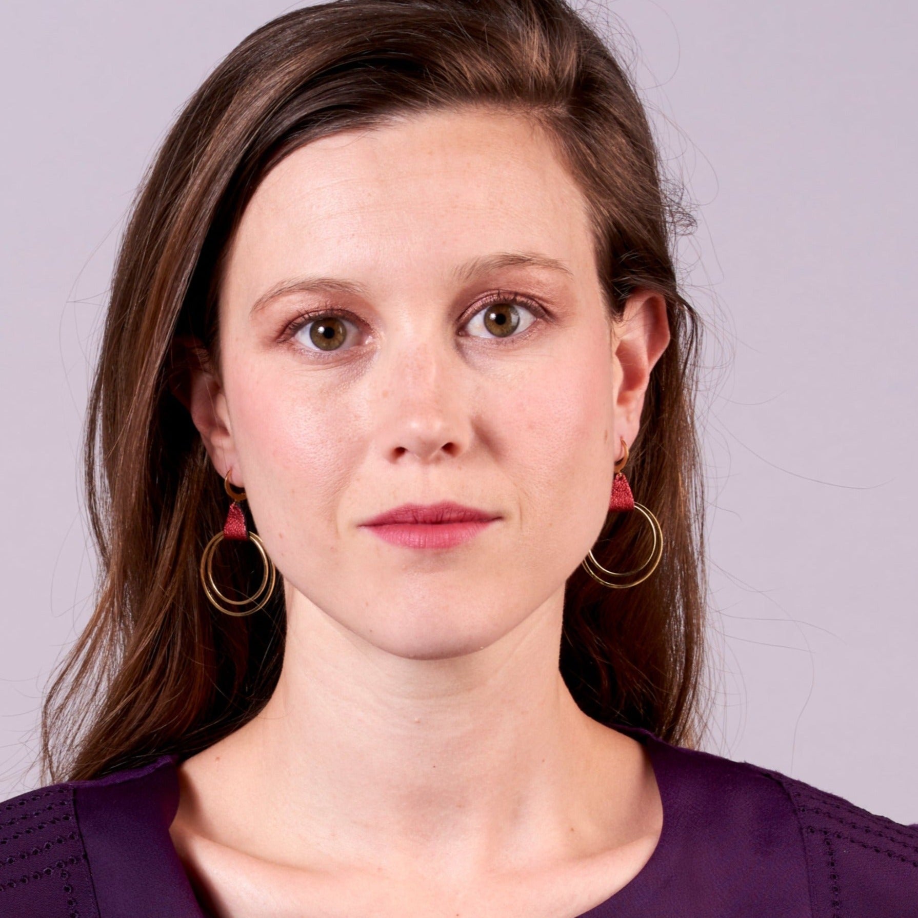 Jeune femme portant les Boucles d'oreilles créoles dorées Nune modèle Vega en cuir rubis métallisé