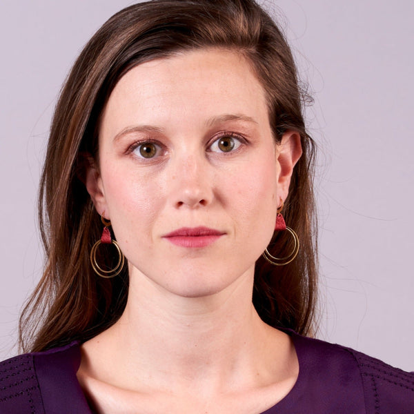 Jeune femme portant les Boucles d'oreilles créoles dorées Nune modèle Vega en cuir rubis métallisé